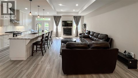 A modern living room with a brown leather couch and a kitchen area with white cabinets.