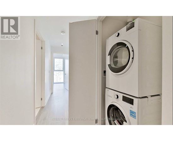 A white washing machine is stacked on top of another in a narrow hallway.