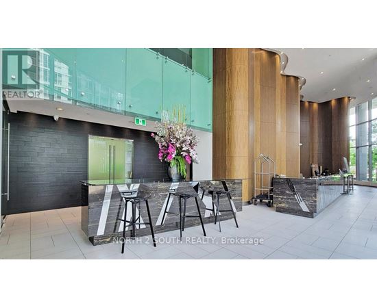 A glass table with chairs is in front of a black wall with a vase of flowers on it.