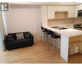 A black couch with pillows sits in a kitchen with white cabinets.