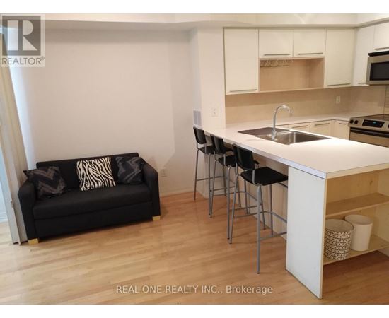 A black couch with pillows sits in a kitchen with white cabinets.