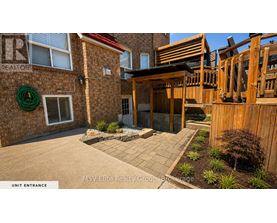 A real estate brochure image of a unit entrance with a brick building and a wooden deck.