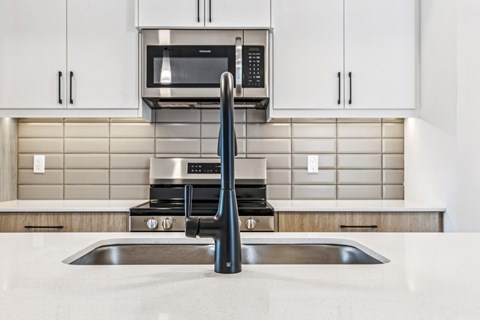 A modern kitchen with a stainless steel sink and a microwave above the stove.