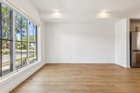A spacious room with wooden flooring and a large window overlooking a street.