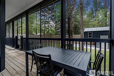 A black table and chairs on a wooden deck with a view of trees.