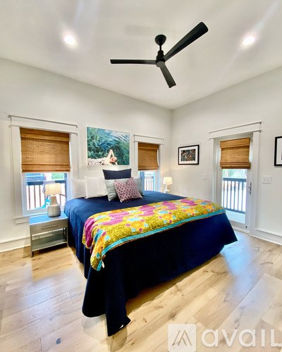 A bedroom with a bed, a ceiling fan, and a painting on the wall.