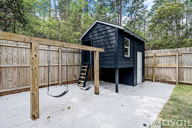 A black shed with a wooden fence and a ladder.