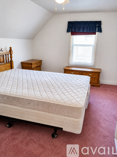 A bedroom with a bed, a dresser, and a window with a blue curtain.
