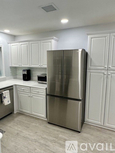 A kitchen with a stainless steel refrigerator and white cabinets.