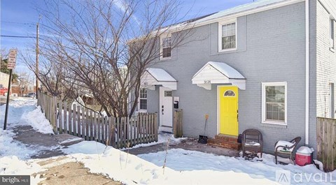 A grey house with a yellow door is surrounded by snow.