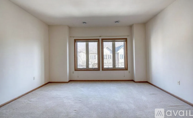A spacious room with a carpeted floor and a large window with a view of a house across the street.