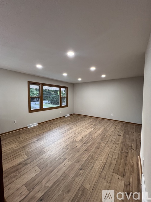 A spacious room with wooden flooring and a window overlooking a snowy landscape.