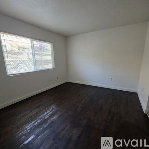 A room with dark wood flooring and a window with blinds.
