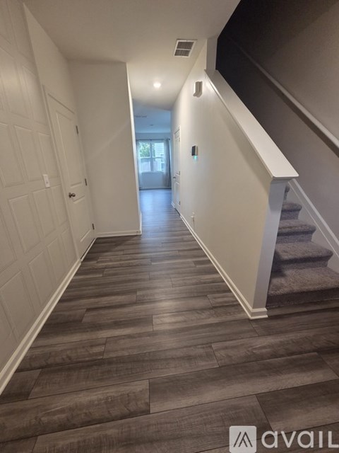A hallway with wooden floors and white walls leading to a door.