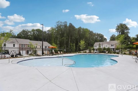 A large outdoor swimming pool surrounded by a concrete patio and residential houses.