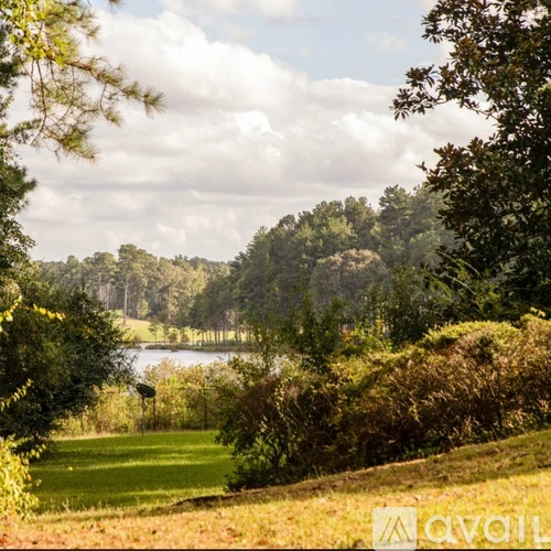 A landscape image of a field with trees and a body of water.