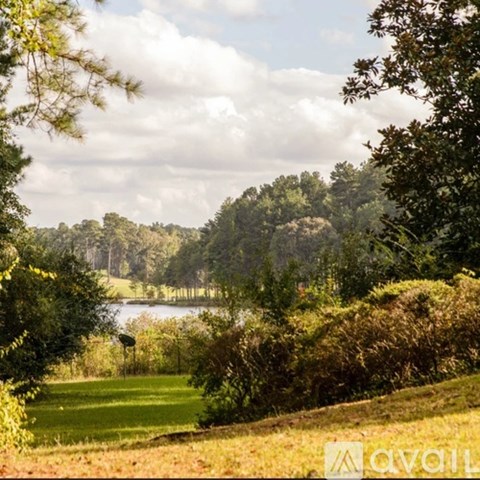 A landscape image of a field with trees and a body of water.