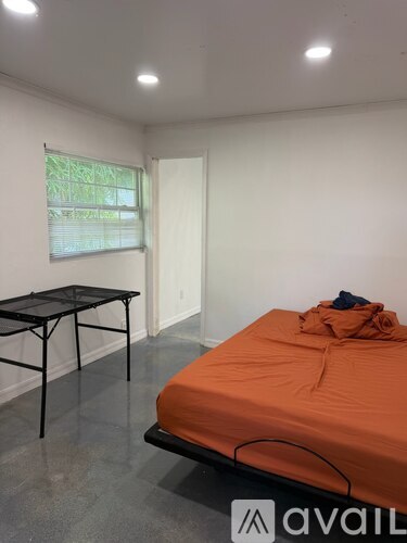 A bedroom with an orange bedspread and a black folding table.