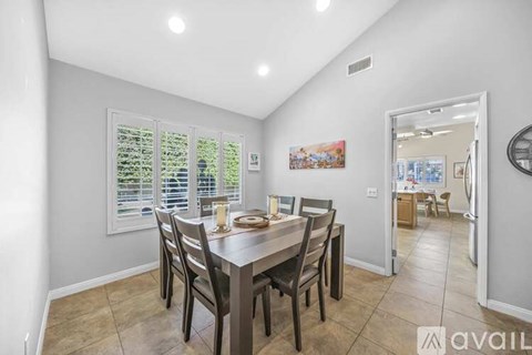 A dining room with a table set for four and a painting on the wall.