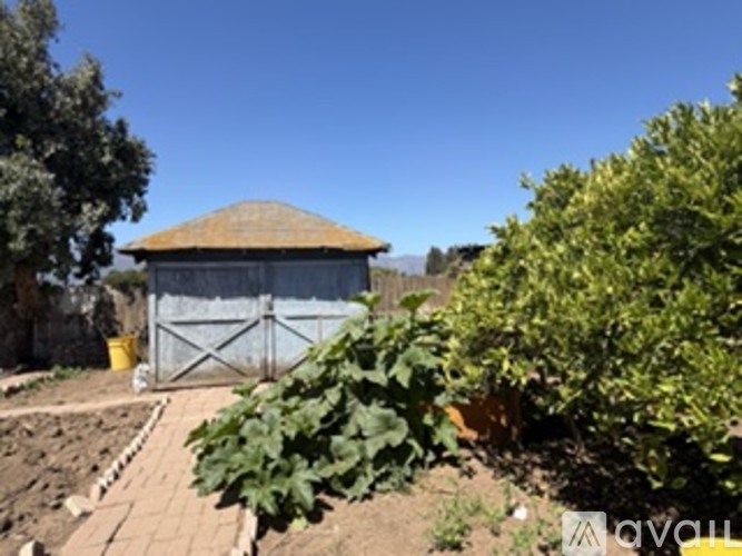 A small building with a brown roof is surrounded by a fence and vegetation.