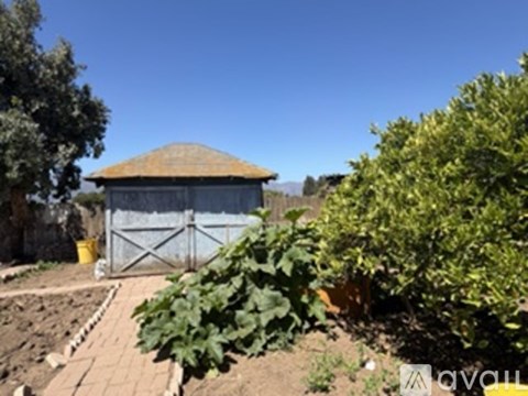 A small building with a brown roof is surrounded by a fence and vegetation.