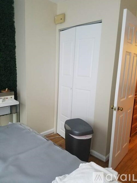 A bedroom with a bed, a trash bin, and a white door.