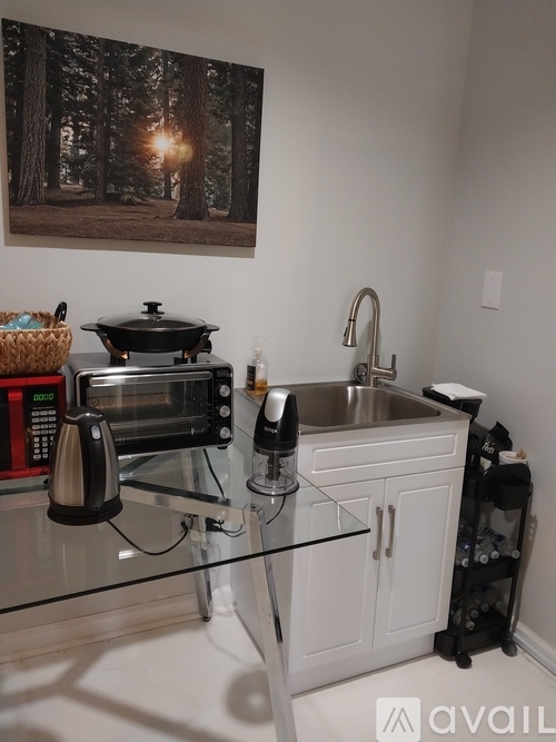 A kitchen with a glass counter top and a painting of a forest on the wall.