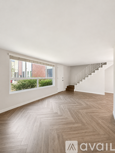 A spacious room with wooden flooring and a staircase leading to another level.