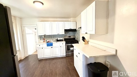 A kitchen with white cabinets and a black trash can.