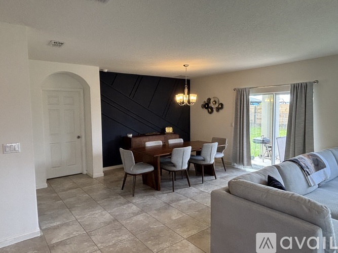 A living room with a grey couch, a dining table with chairs, and a sliding glass door.