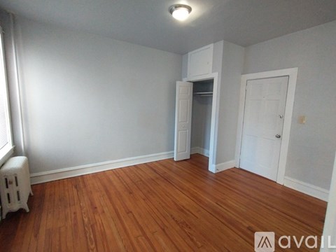 A room with wooden floors and white walls, with a small white cabinet and a door on the right.