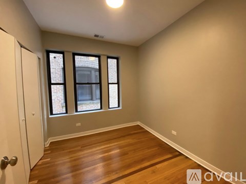 A room with wooden floors and a window with a view of a brick building.