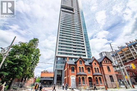 A tall building with a glass facade stands next to a row of red brick houses.