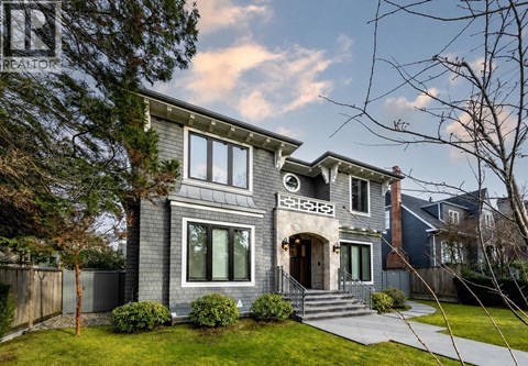 A grey house with a front yard and a tree.