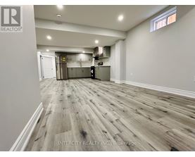 A spacious room with wooden flooring and a kitchen area in the background.