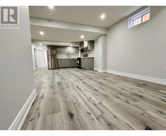 A spacious room with wooden flooring and a kitchen area in the background.