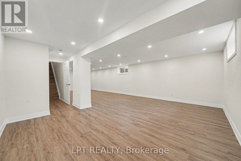 A spacious room with wooden flooring and white walls, with a logo that reads "REALTOR" in the top left corner.