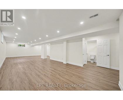 A spacious room with wooden flooring and white walls, with a toilet visible in the corner.