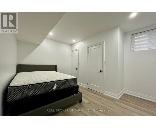 A bedroom with a bed, wooden floors, and white walls.