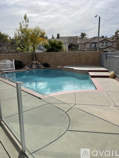 A pool surrounded by a concrete patio and a stone wall.