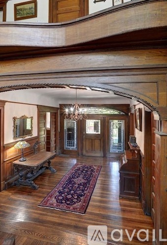 A hallway with a chandelier, a bench, and a rug.