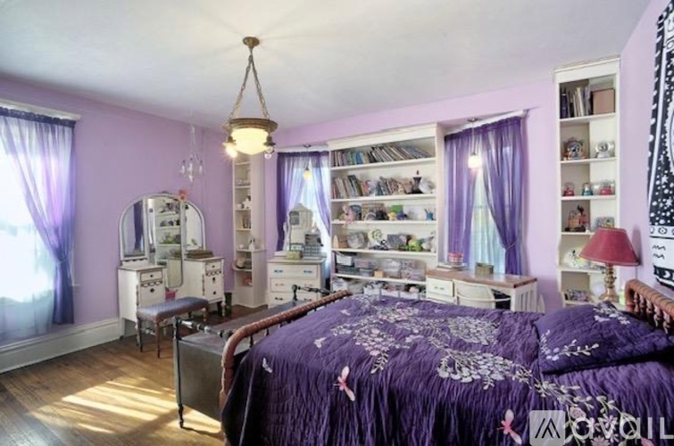A bedroom with a purple bedspread and a bed in the center of the room.