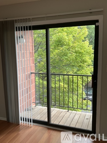 A balcony with a black railing and a view of a green tree and a brick building.