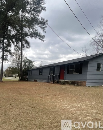A house with a grey exterior and a red door is surrounded by a grassy area.