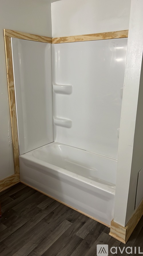 A white bathroom cabinet with a gold frame is installed in a room with wooden flooring.