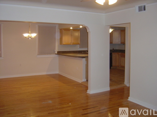 A room with wooden floors and a kitchen area in the background.