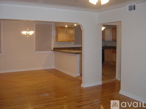 A room with wooden floors and a kitchen area in the background.