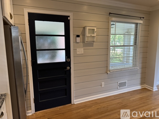 A black door with a glass window is in a room with wooden floors and white walls.