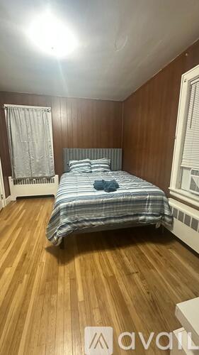 A bedroom with a bed, wooden floor, and a window with blinds.