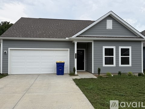 A house with a garage and a blue trash bin in front.